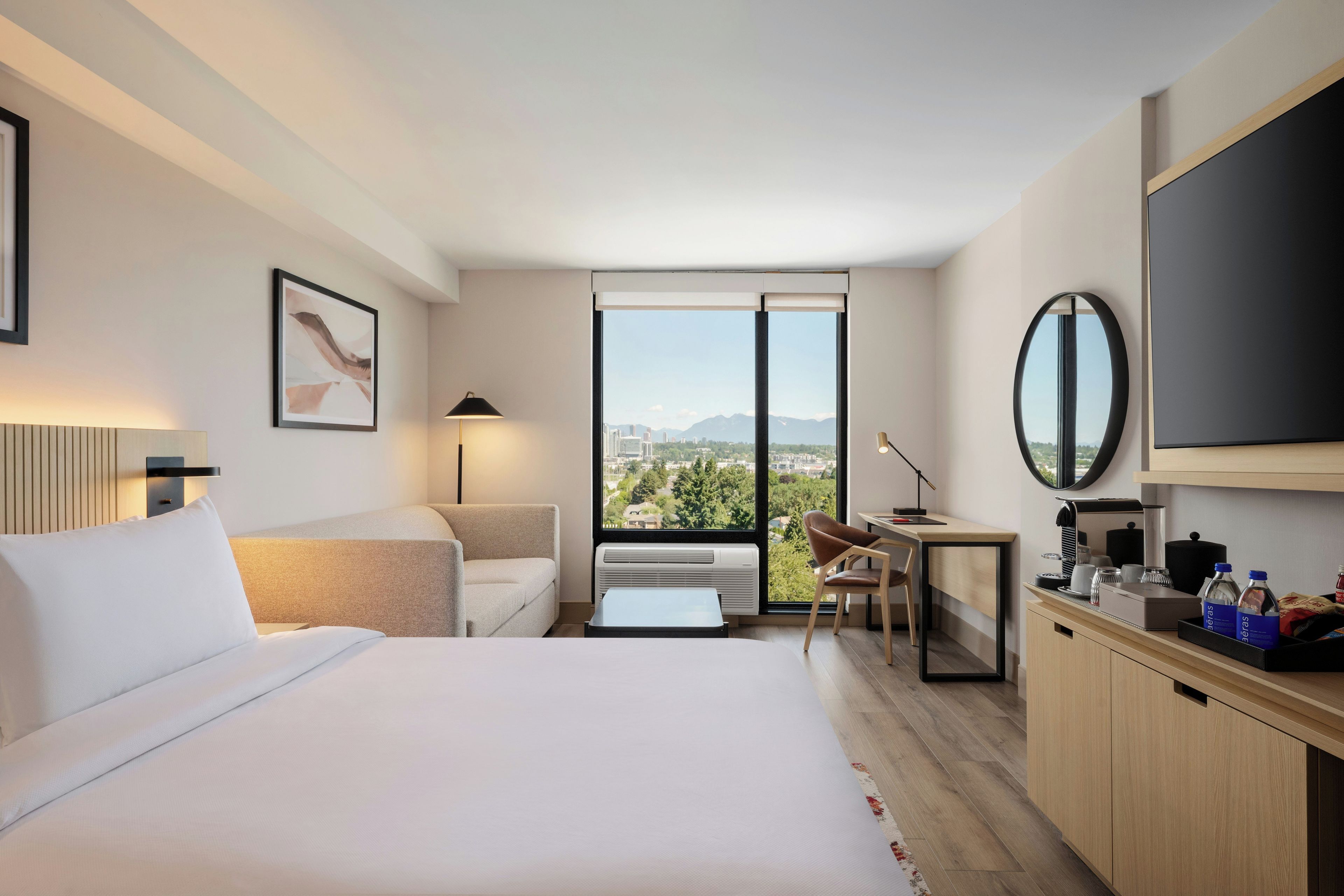 Habitación de hotel moderna con cama, escritorio, silla, televisor y vista a la ciudad.