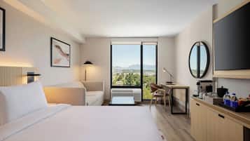 Habitación de hotel moderna con cama, escritorio, silla, televisor y vista a la ciudad.