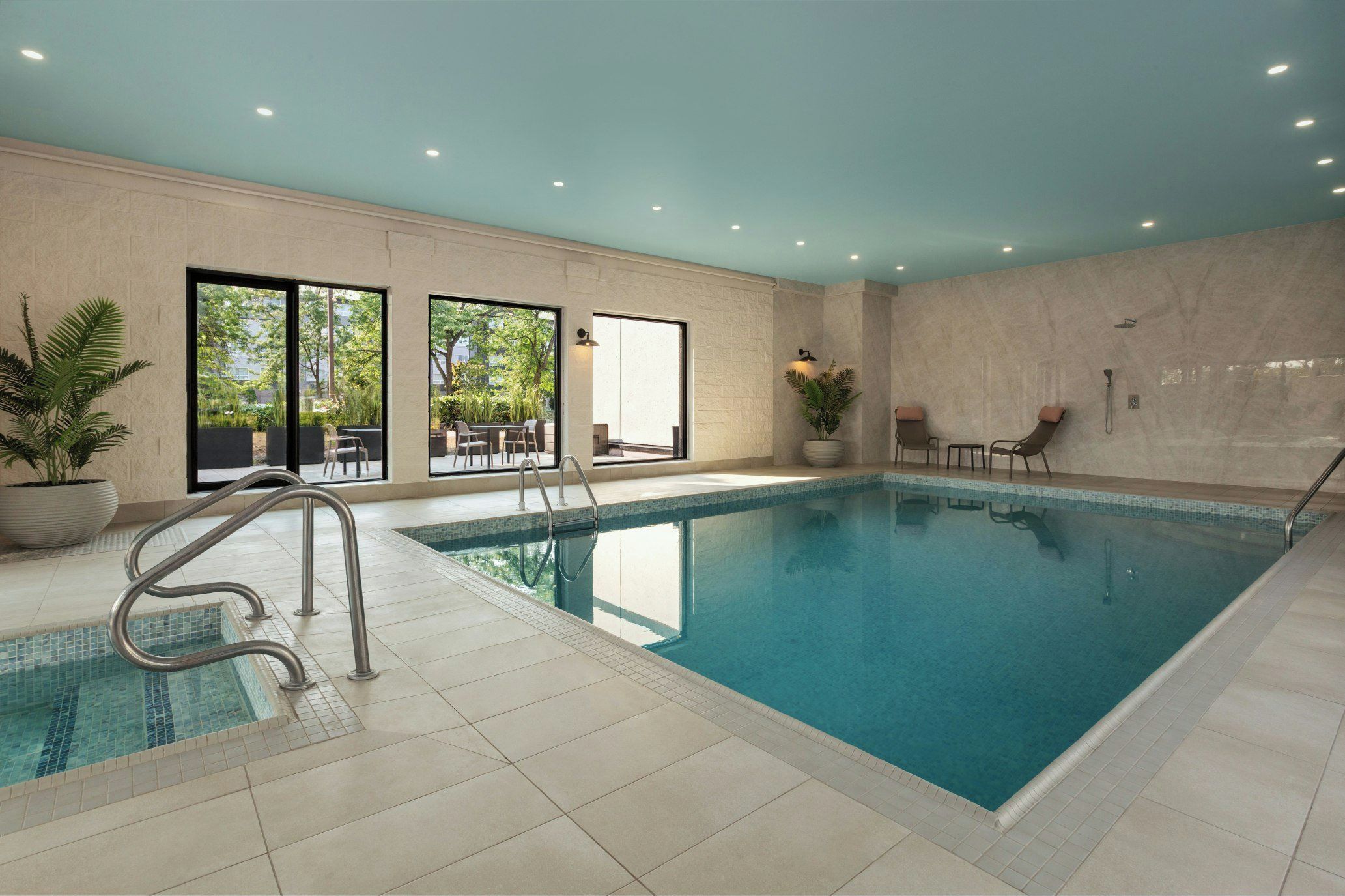 An indoor swimming pool with a clear view of the outside, a seating area, and a shower area.