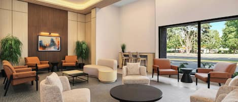 Un hall d’entrée moderne, doté d’un espace détente avec des fauteuils, une table basse et une grande fenêtre donnant sur l’extérieur.