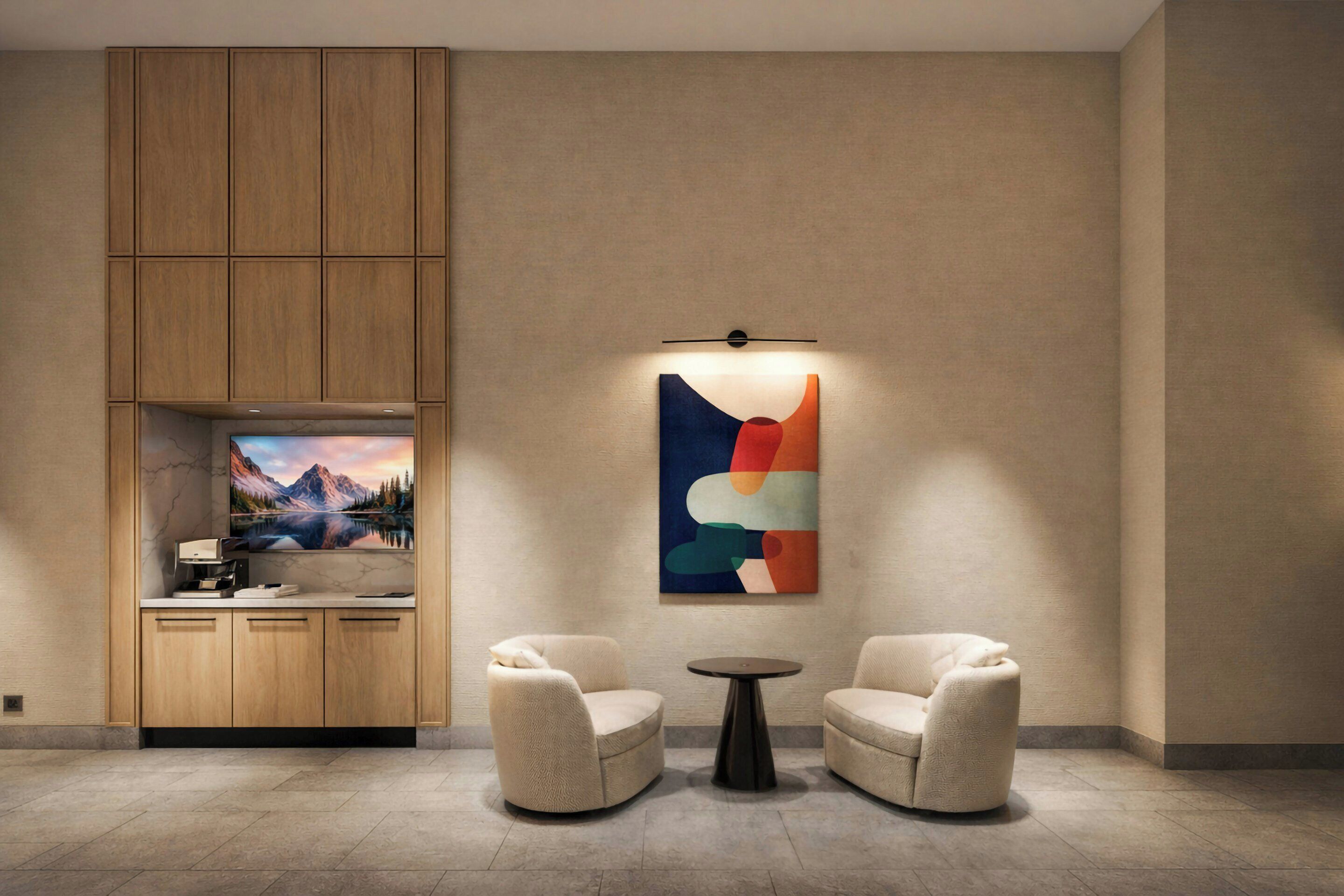 A modern room with a wooden cabinet, a flat-screen TV, two armchairs, a small round table, and a colorful abstract painting.