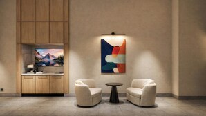 A modern room with a wooden cabinet, a flat-screen TV, two armchairs, a small round table, and a colorful abstract painting. - Red Roof Inn PLUS+ Vancouver Airport (Richmond)