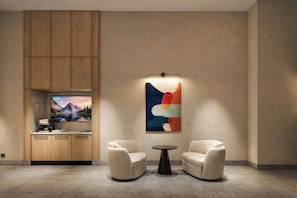 Habitación moderna con un armario de madera, un televisor de pantalla plana, dos sillones, una mesita redonda y un cuadro abstracto colorido.