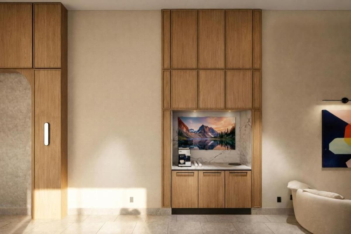 A modern kitchen with wooden cabinets, a built-in island with a painting, and a seating area with a chair.