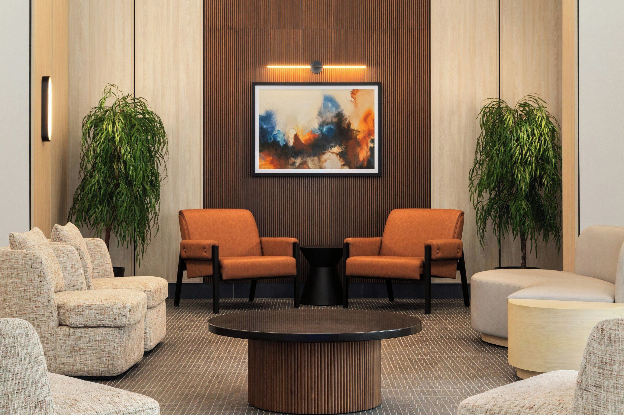 A lobby with two orange armchairs, a round coffee table, and a large abstract painting on the wall.