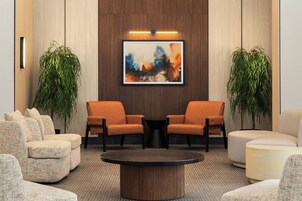 A lobby with two orange armchairs, a round coffee table, and a large abstract painting on the wall.