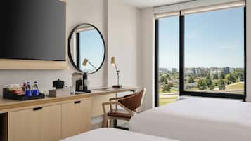 A hotel room with a large bed, a desk with a chair, a flat-screen TV, a mirror, and a window with a city view.
