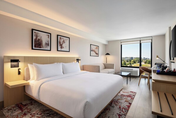Habitación de hotel con una cama grande, un escritorio, una silla, un televisor y una ventana con vista a la ciudad.
