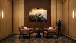 A modern interior with two leather chairs, a round table, a large abstract painting, and wooden paneling. - Red Roof Inn PLUS+ Vancouver Airport (Richmond)