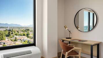 Une chambre moderne dotée d’une grande fenêtre, d’un bureau, d’une chaise, d’un miroir rond et d’un appareil de climatisation.