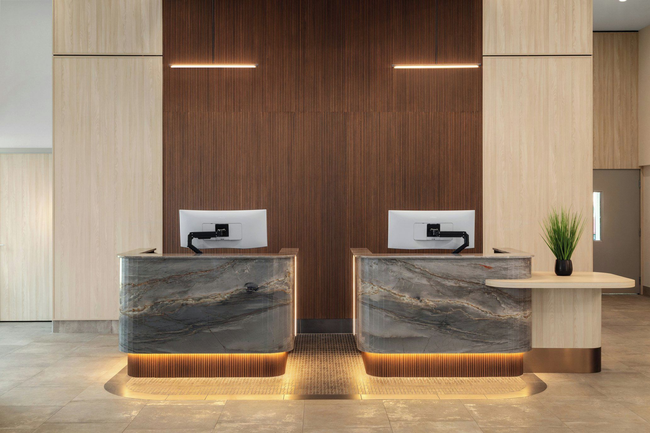 A reception desk with two computer monitors, a potted plant, and a wooden panel wall.