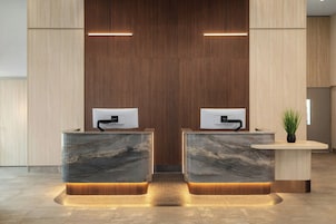 A reception desk with two computer monitors, a potted plant, and a wooden panel wall.