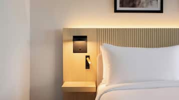 Quarto de hotel com cama bem arrumada, mesa de cabeceira com abajur e luminária na parede.