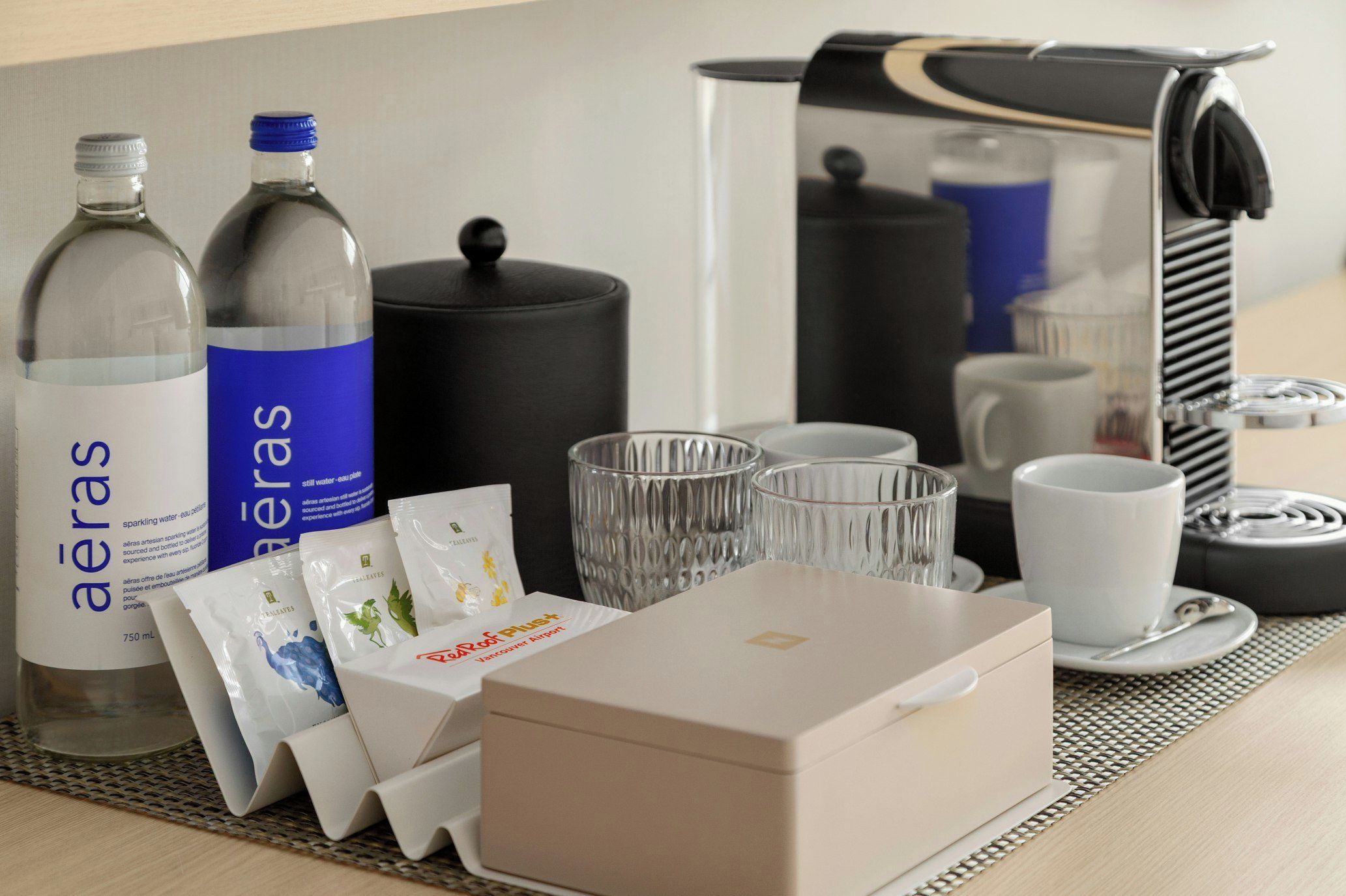 Ein Hotelzimmer mit Kaffeemaschine, zwei Wasserflaschen, Taschentuchbox und einem Glas-Set.