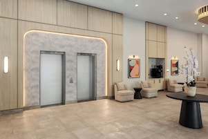 Un lobby moderno con dos ascensores, una máquina de café y una zona de estar con una mesa redonda.