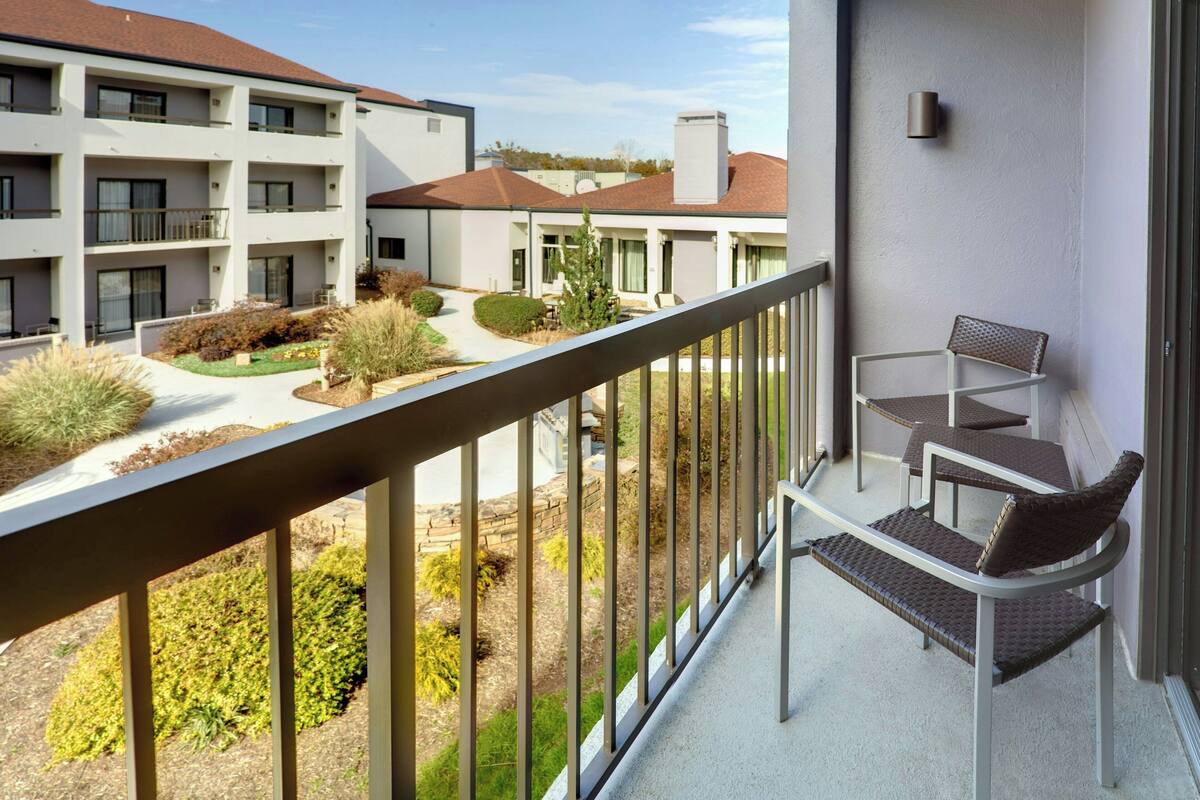 Un balcon avec deux fauteuils en osier et une petite table, donnant sur une cour intérieure avec un bâtiment en arrière-plan.