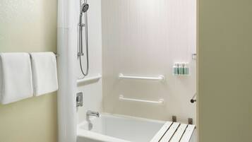 A bathroom with a white bathtub, a showerhead, and handrails.