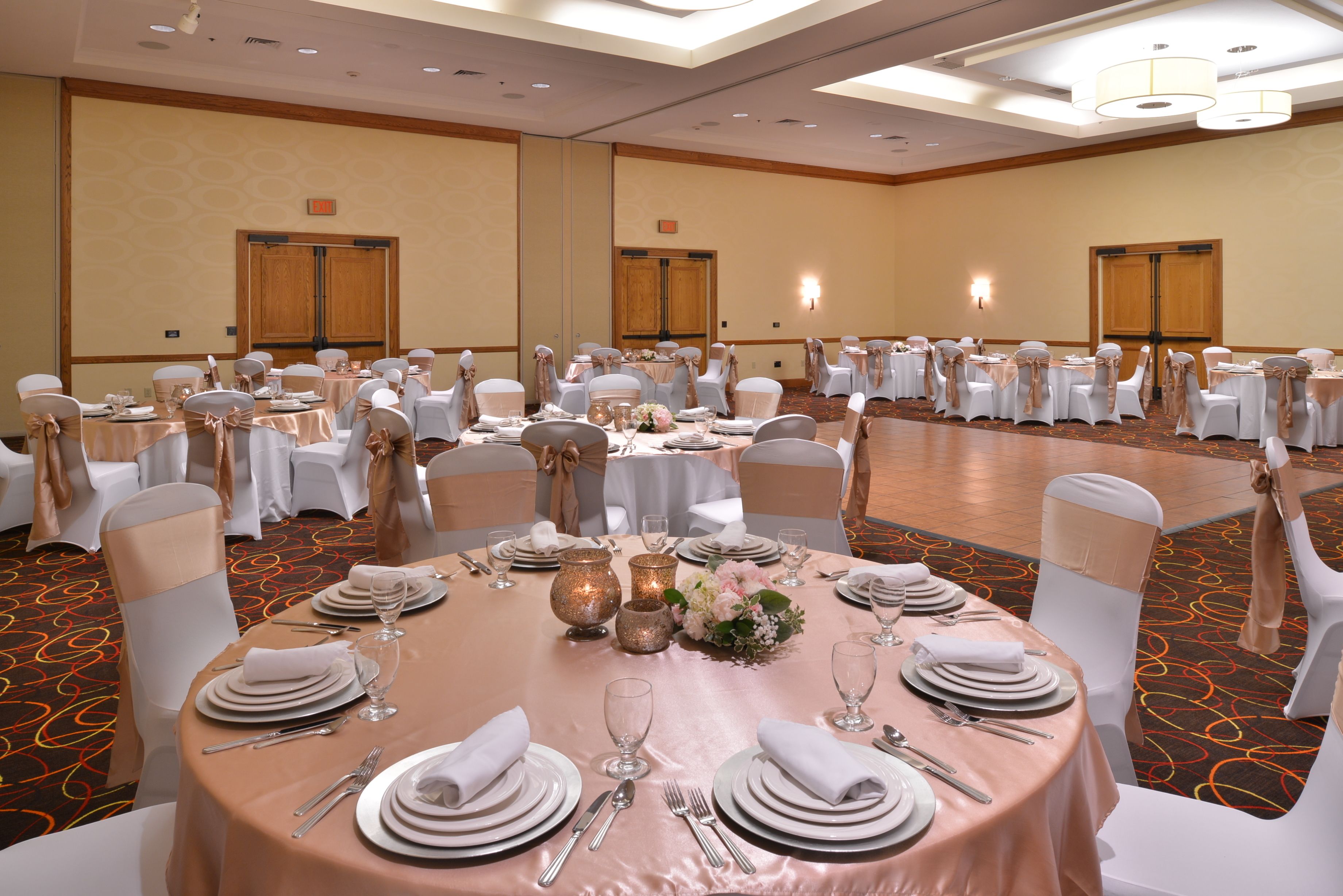 A banquet hall with round tables set for a formal event, featuring white chairs, tablecloths, and floral centerpieces.