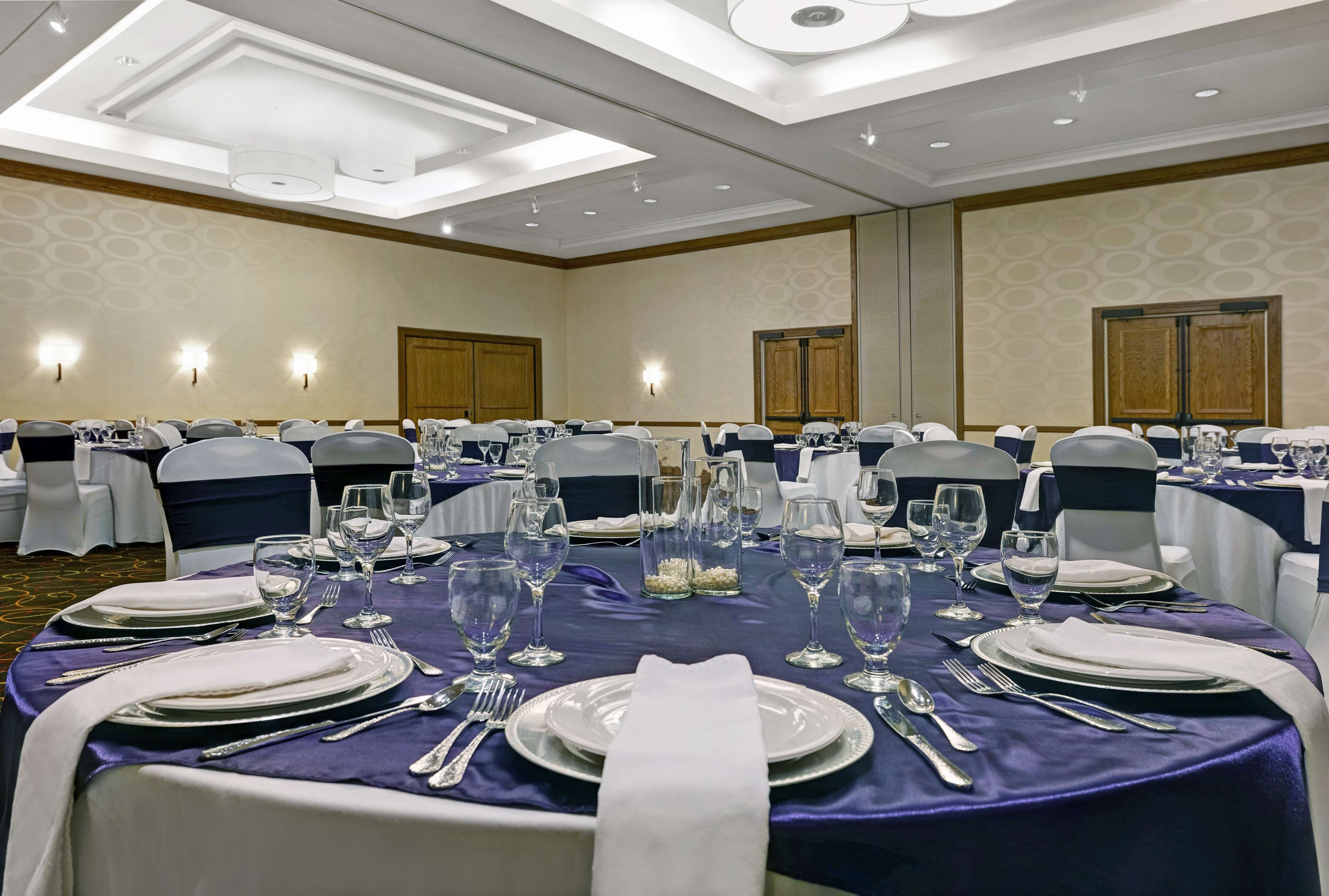 A banquet hall with round tables set for dining, equipped with white tablecloths, silverware, and glassware.
