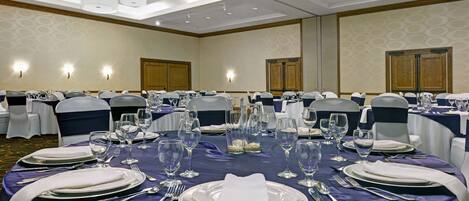 A banquet hall with round tables set for dining, equipped with white tablecloths, silverware, and glassware.