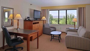 A hotel room with a desk, office chair, sofa, and a TV on a wooden cabinet.