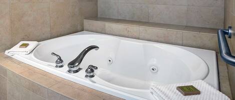 Una bañera grande y blanca con dos llaves, un asiento incorporado y un pequeño jabonera.