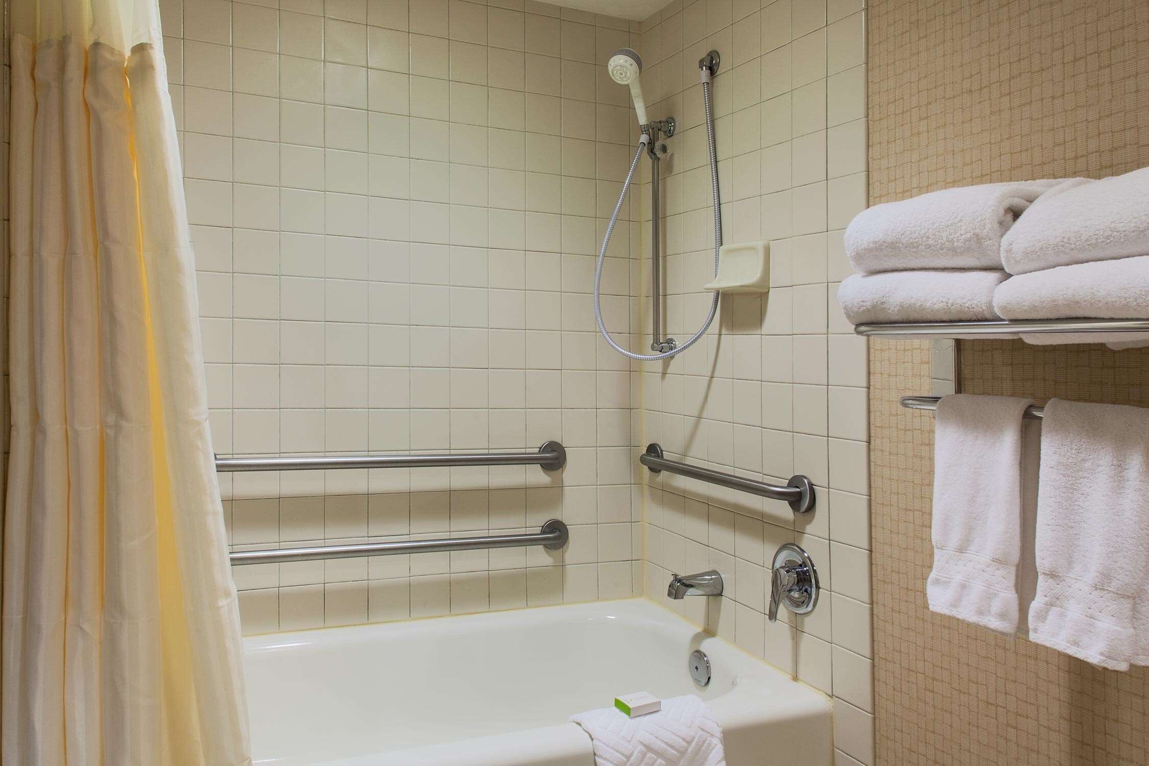 Un baño con bañera, barras de apoyo, ducha y toallero con toallas.