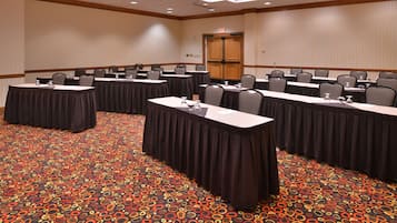 Un salón de conferencias con largas mesas, sillas y una alfombra estampada.