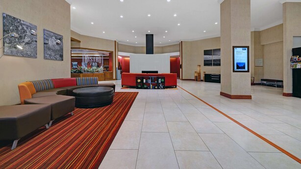 A spacious lobby with a central seating area, a reception desk, and a digital information screen.