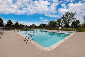 A rectangular swimming pool with a tiled deck, surrounded by a metal fence, and trees in the background. - Doubletree Hotel Grand Junction (Grand Junction)