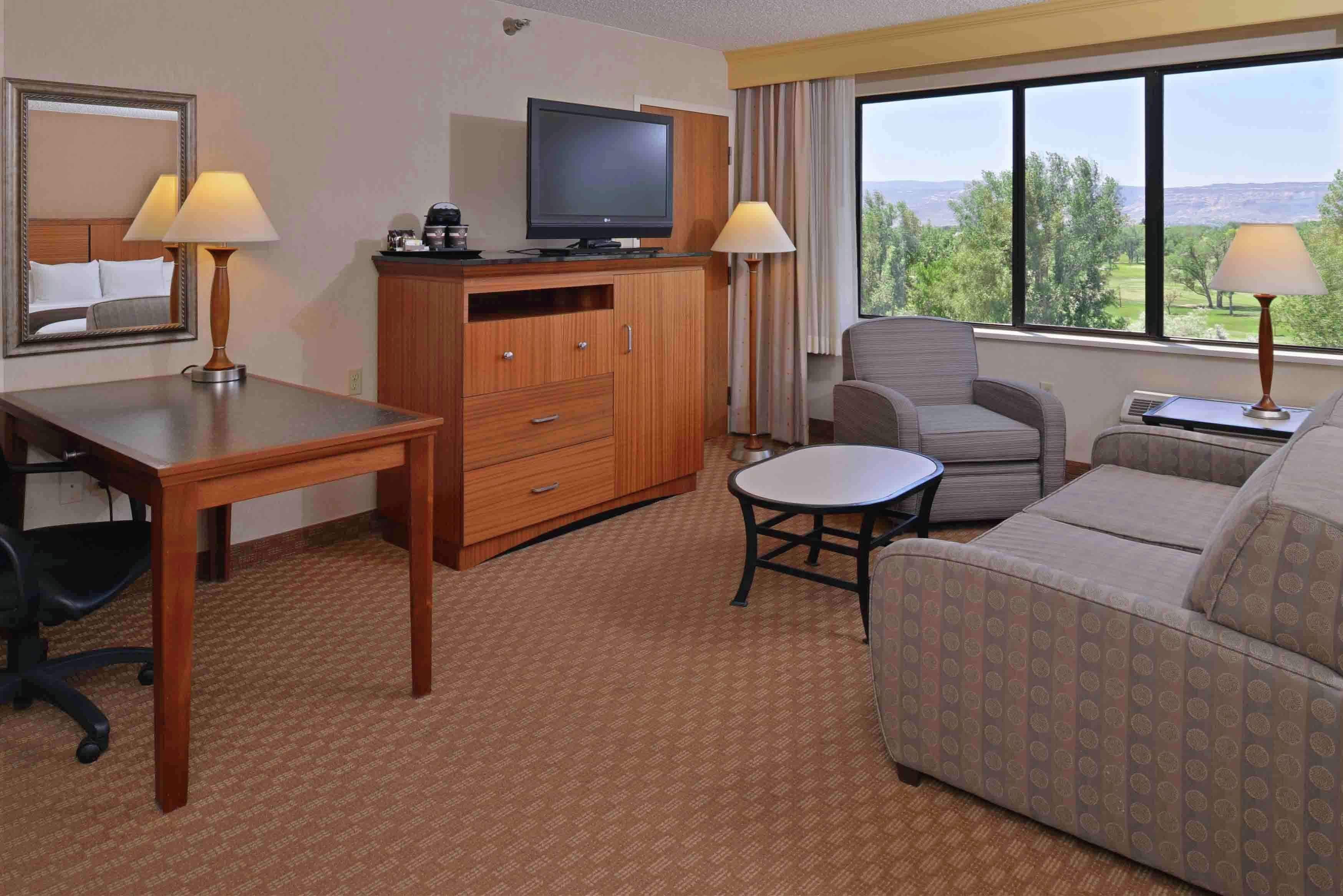 A hotel room with a wooden desk, a television, a sofa, and a view of the outdoors.