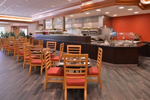 A restaurant with wooden chairs and tables, a counter with a cash register, and a kitchen area with ovens and a stove. - Doubletree Hotel Grand Junction (Grand Junction)