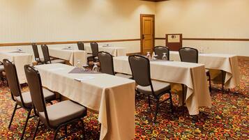 A conference room with multiple tables and chairs, carpeted floor, and a door in the background.