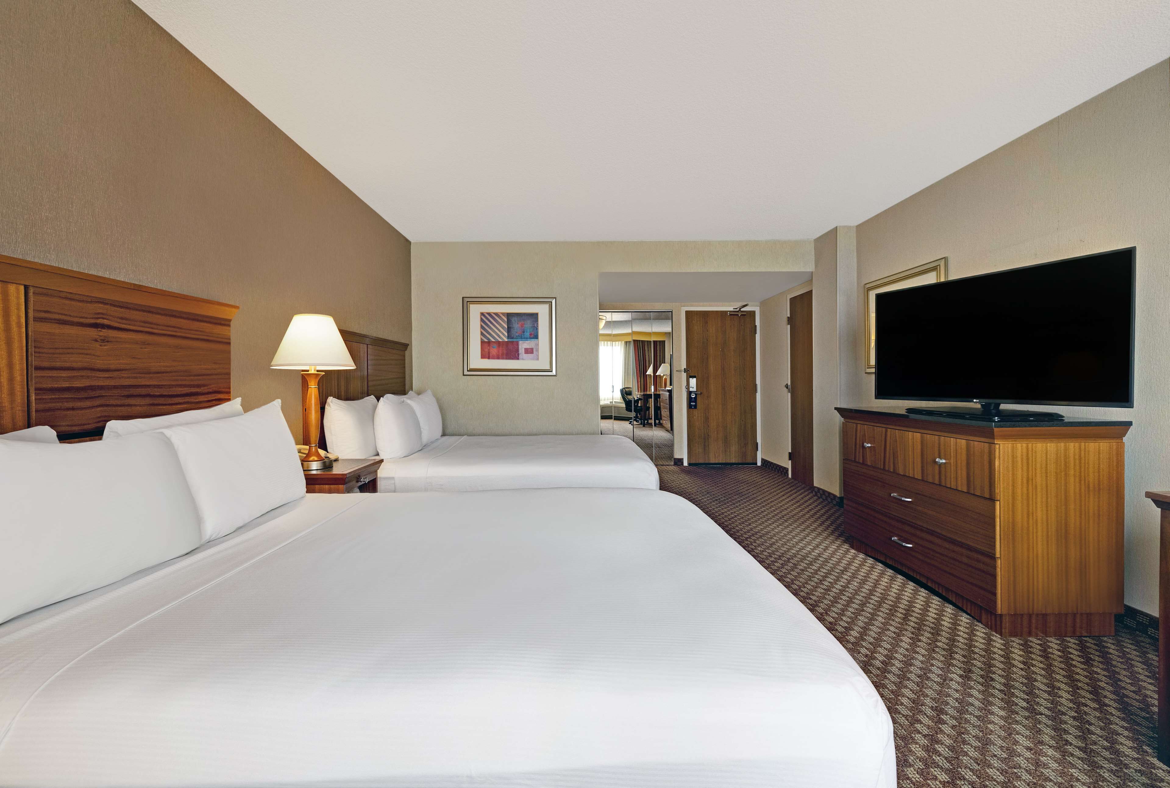 A hotel room with two beds, a TV, a lamp, and a wooden dresser.