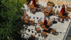 An outdoor patio area with multiple wooden tables and chairs, some with red umbrellas.