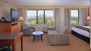 A hotel room with a bed, a sofa, a small table, a TV, and a desk with a lamp.