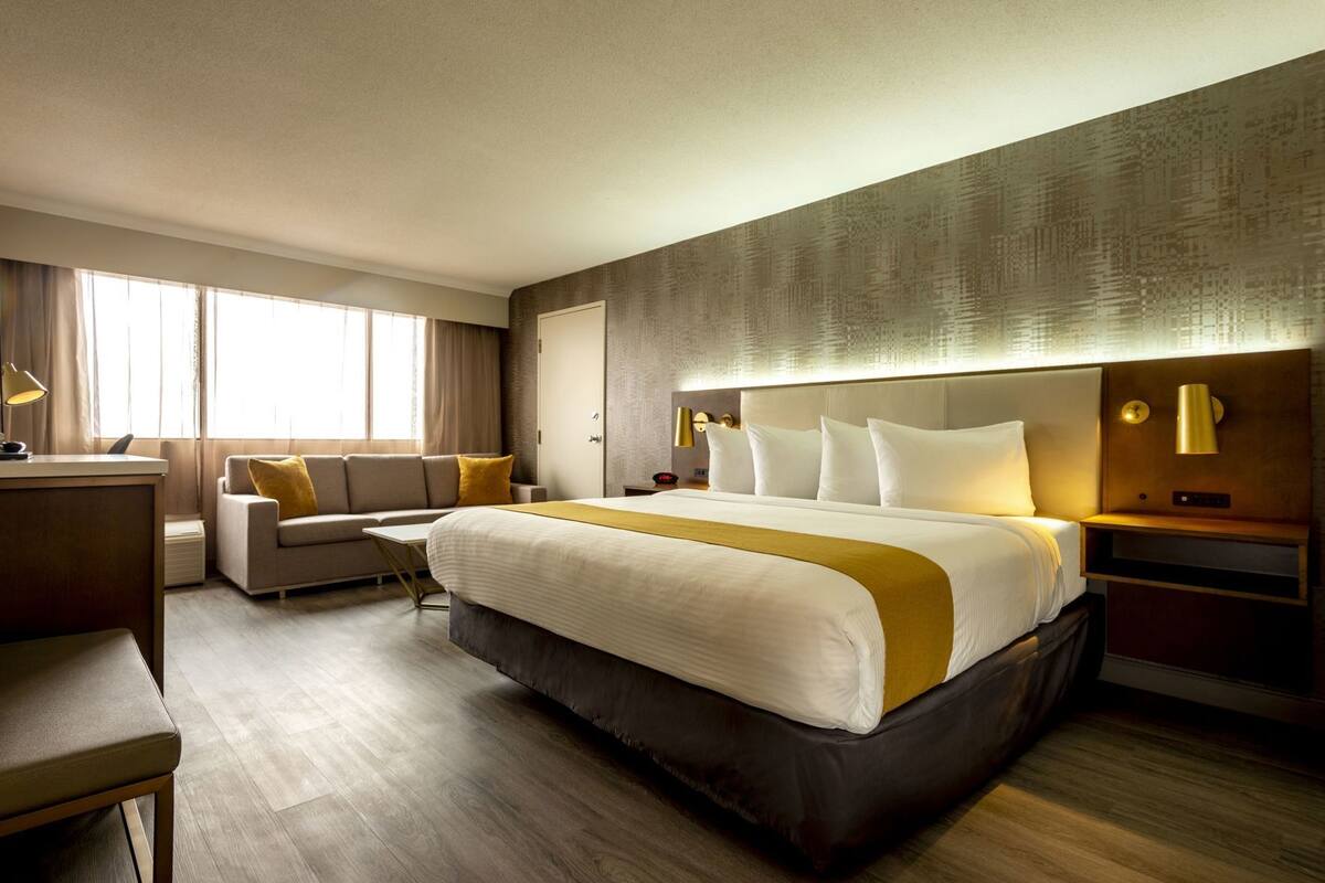 A hotel room with a large bed, a desk, a sofa, and a nightstand with lamps.