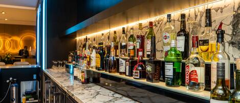 Een bar met een marmeren aanrecht en verschillende flesjes drank.