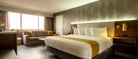 A hotel room with a large bed, a sofa, a desk, and a nightstand with lamps.