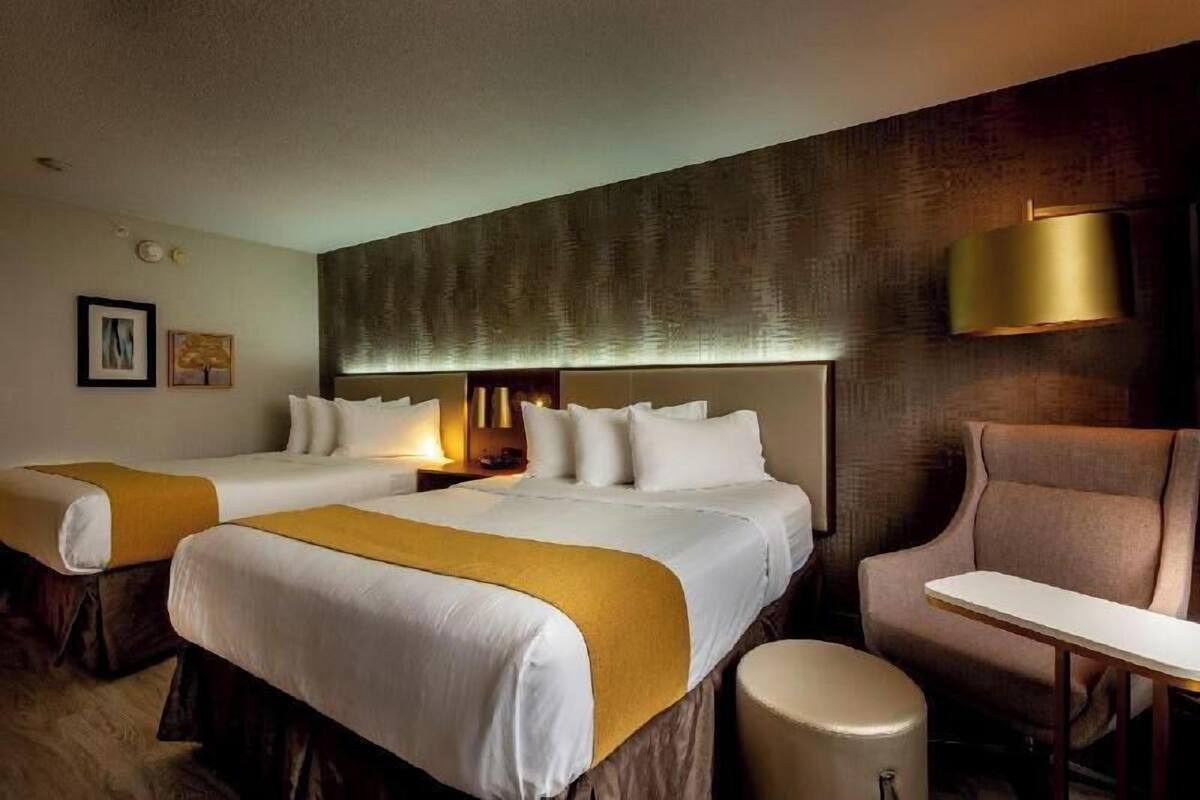 A hotel room with two beds, a desk, a chair, and a round ottoman.
