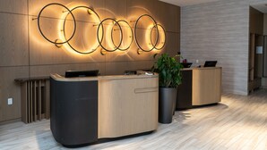 A reception area with a wooden reception desk, a potted plant, and a wall-mounted circular light fixture. - Atlantica Hotel Halifax (Halifax)