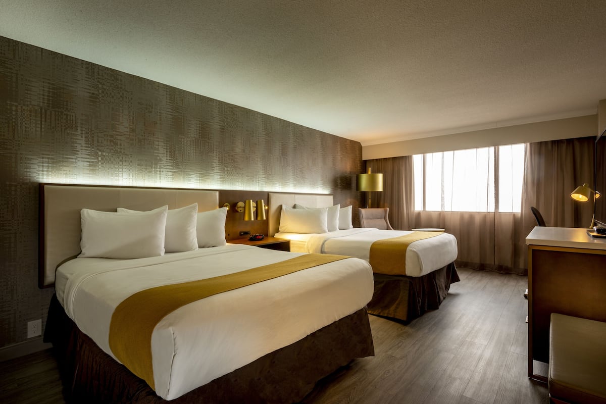 A hotel room with two beds, a desk, and a large window with curtains.