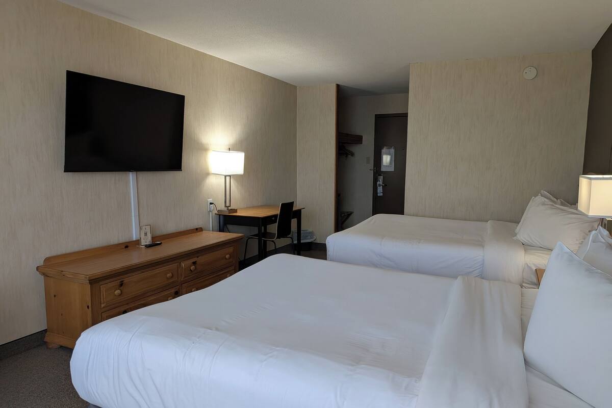 Una habitación de hotel con dos camas, un escritorio, una silla, un televisor y una lámpara.
