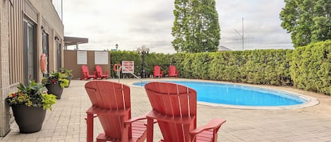 Piscina com cadeiras vermelhas e plantas em vasos, rodeada por um pátio de tijolos e um viveiro.