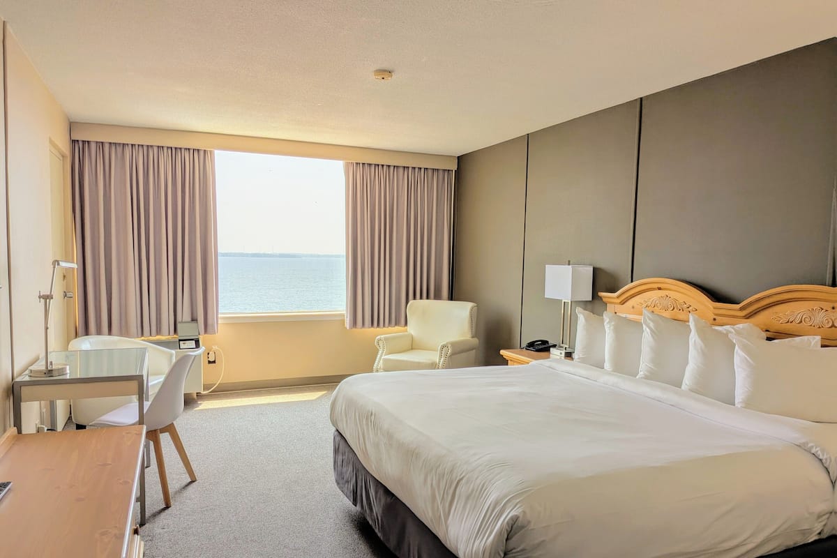 Habitación de hotel con una cama grande, un escritorio, una silla y vista al mar a través de la ventana.