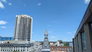 Une vue urbaine avec un grand immeuble imposant, un bâtiment historique doté d’un toit en forme de flèche, et une rivière en arrière-plan.