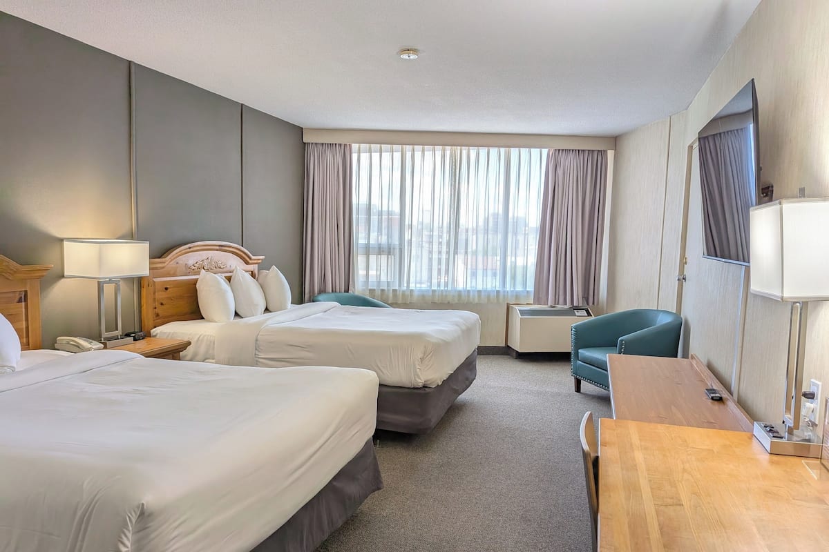 Habitación de hotel con dos camas, un escritorio, una silla, una lámpara y una ventana con cortinas.