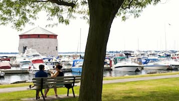 Un paseo marítimo bordeado de árboles, con una torre histórica y un puerto deportivo lleno de barcos.