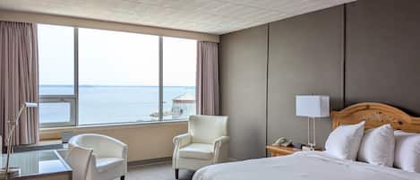 Habitación de hotel con una cama grande, dos sillones, un escritorio y vista al mar.