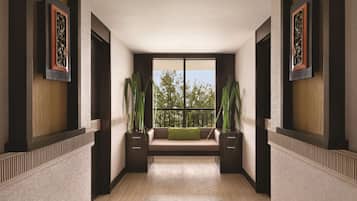 A hallway with a bench, framed artwork, and potted plants.